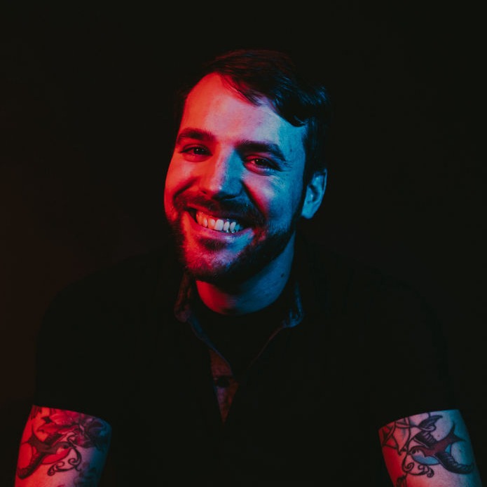 white man with dark hair, beard, and tattoos smiles to camera