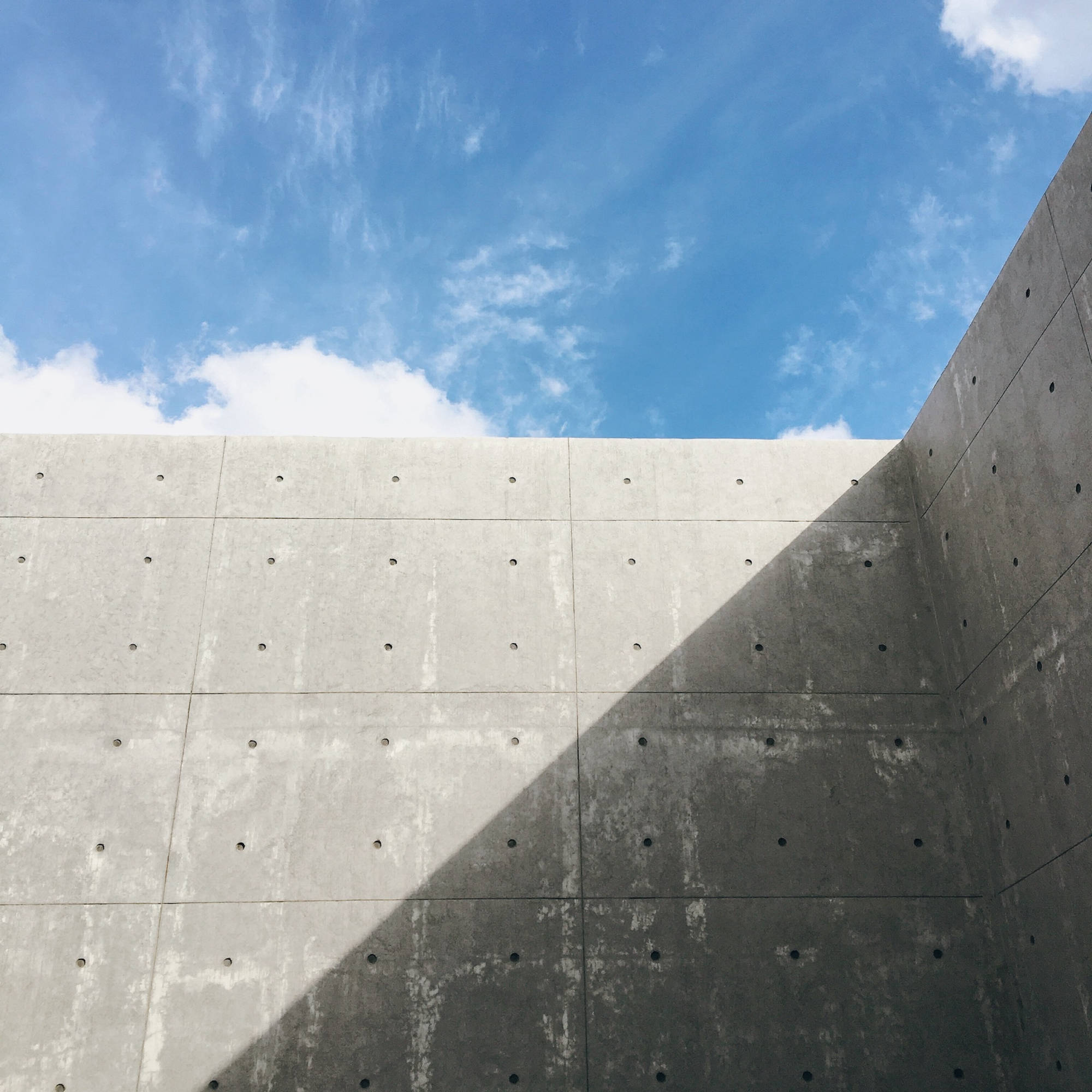 High concrete wall with blue cloudy sky peeking above